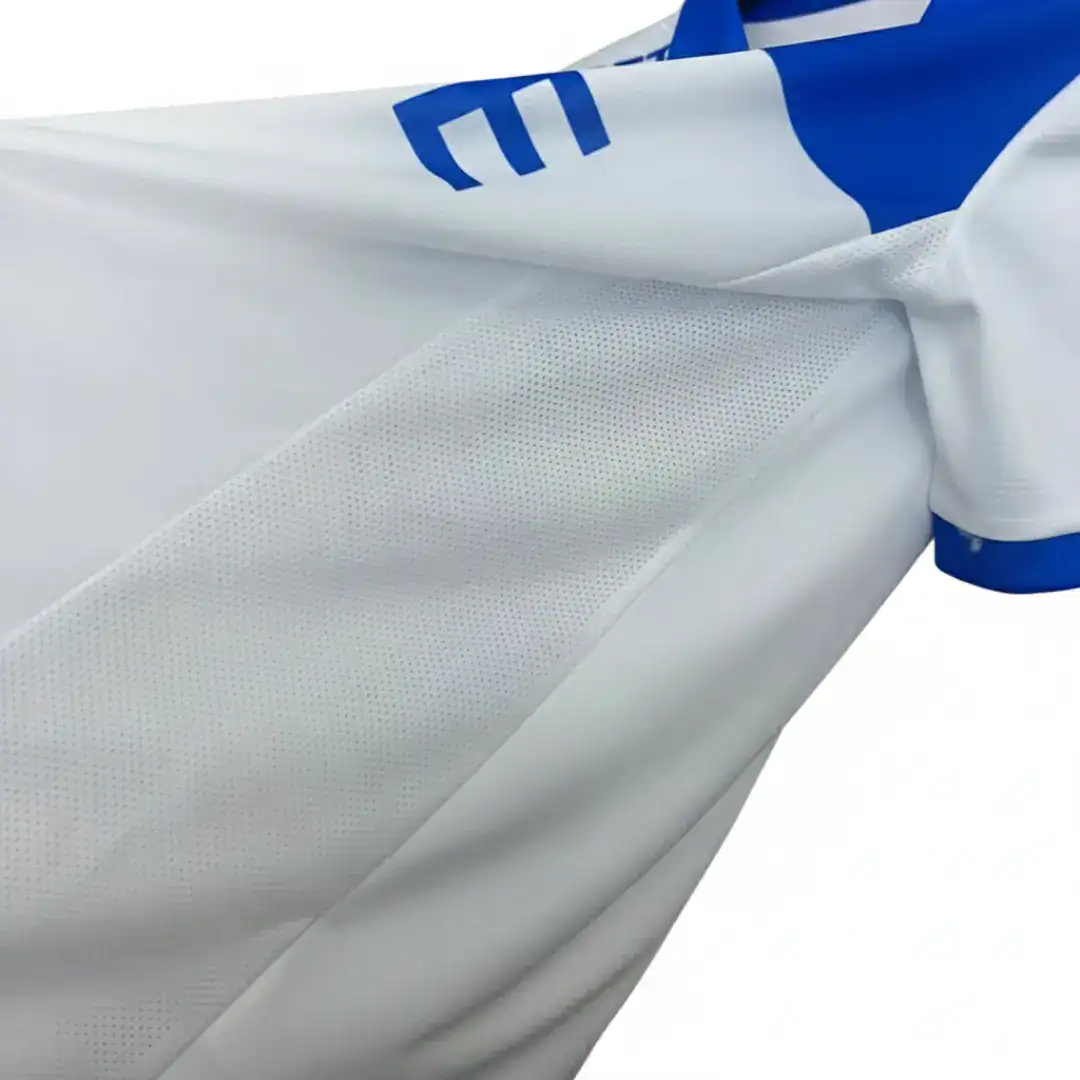 Primer plano detallado de una camiseta deportiva blanca, destacando la textura de tela de malla transpirable y un detalle azul con la letra 'E' visible, junto a un borde azul en la manga.
