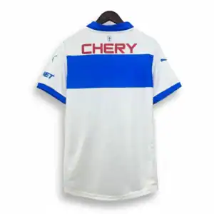 camiseta-futbol-blanca-franja-azul-chery-espalda Camiseta de fútbol blanca con una franja horizontal azul en el medio, cuello azul y el logo rojo "CHERY" en la espalda, colgada en un gancho de madera sobre un fondo blanco.