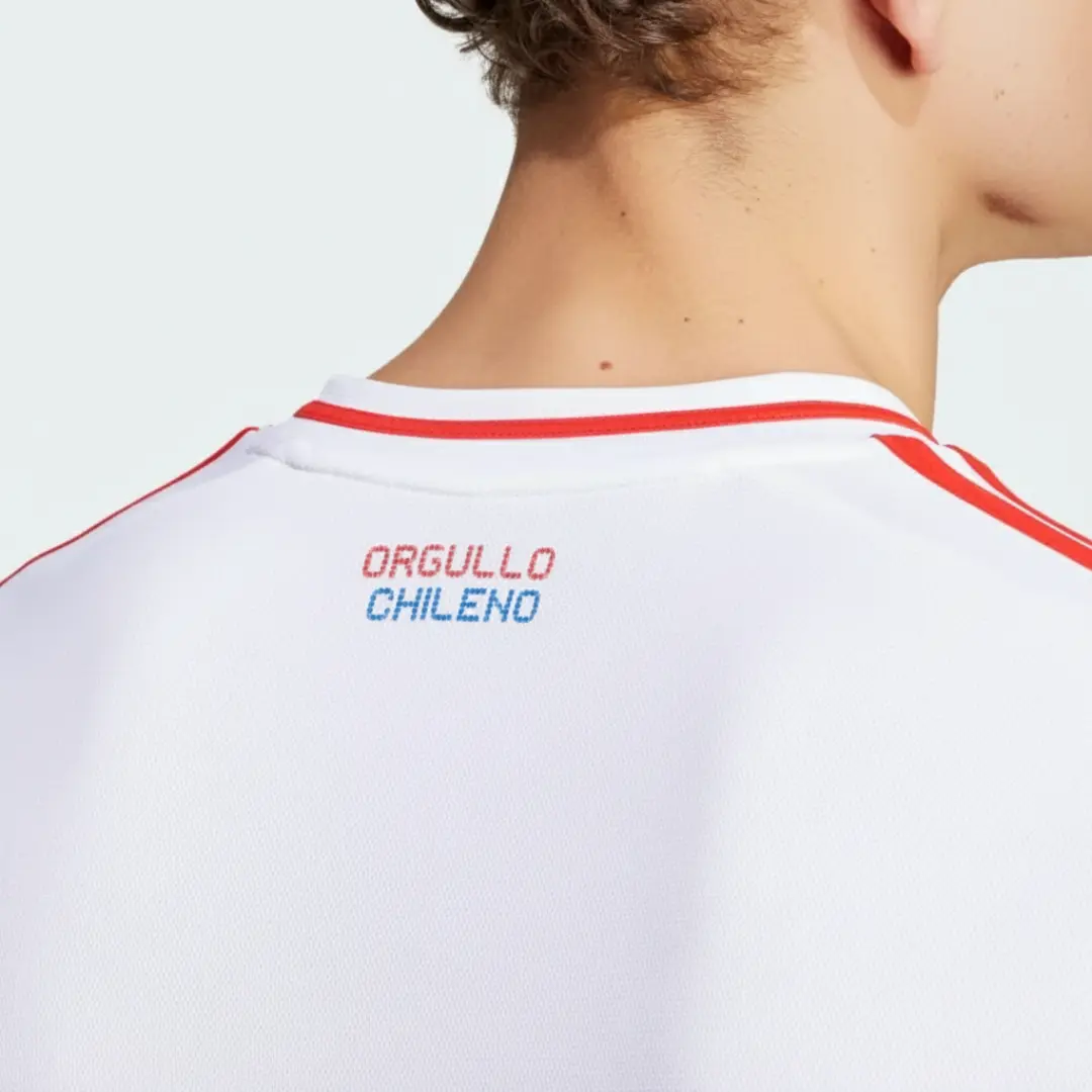 Primer plano de la espalda de un hombre vistiendo una camiseta deportiva blanca con rayas rojas en los hombros y el borde del cuello, y la inscripción 'ORGULLO CHILENO' en letras rojas y azules en la parte superior.