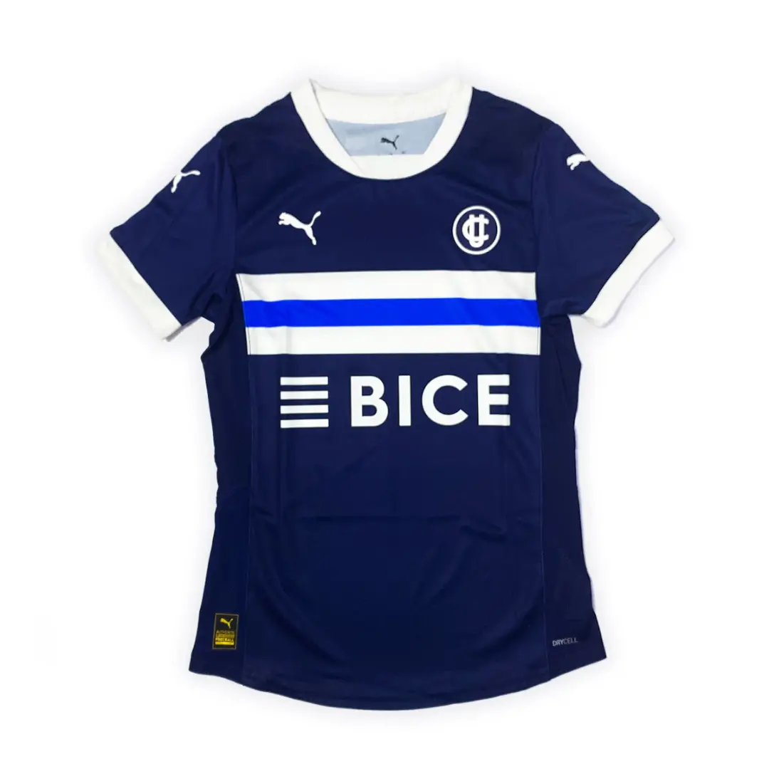 Camiseta de fútbol azul marino de la marca Puma, con un diseño que incluye una franja azul brillante sobre una blanca en el pecho, el escudo de un club en blanco a la izquierda, el logotipo de Puma a la derecha y en las mangas, y el patrocinio de 'BICE'.