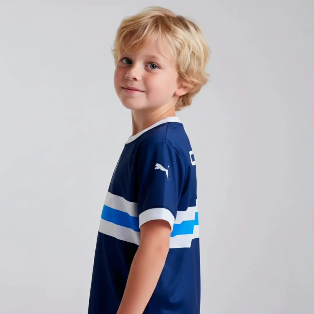 Vista trasera de un niño con una camiseta de fútbol azul marino que lleva el logo 'CHERY' en blanco, franjas horizontales blancas y azules en el centro, y el logo de Puma en la manga derecha.