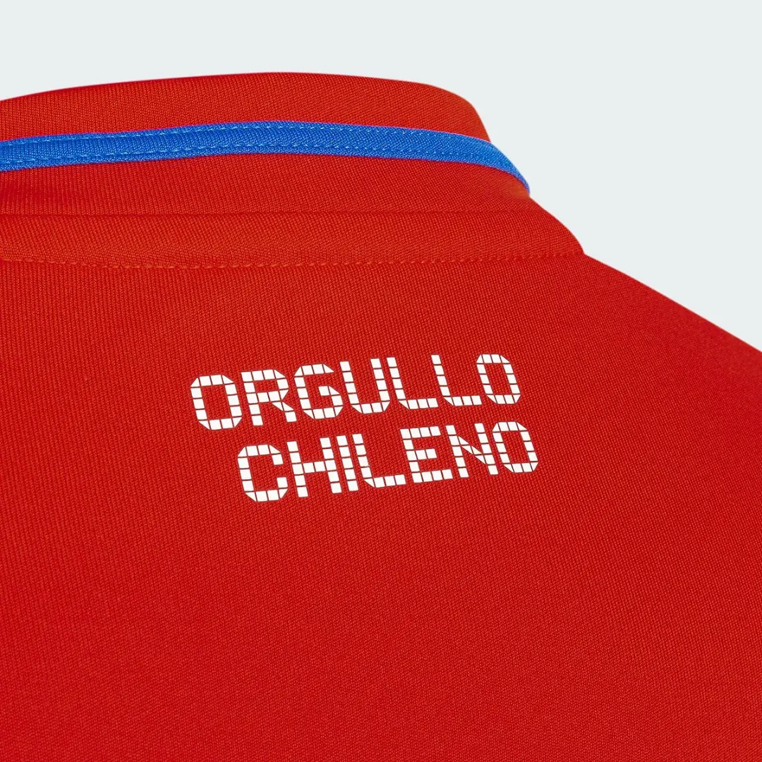 Detalle de la parte trasera de una camiseta roja con la frase "ORGULLO CHILENO" en letras blancas pixeladas, y una banda azul visible en el interior del cuello.