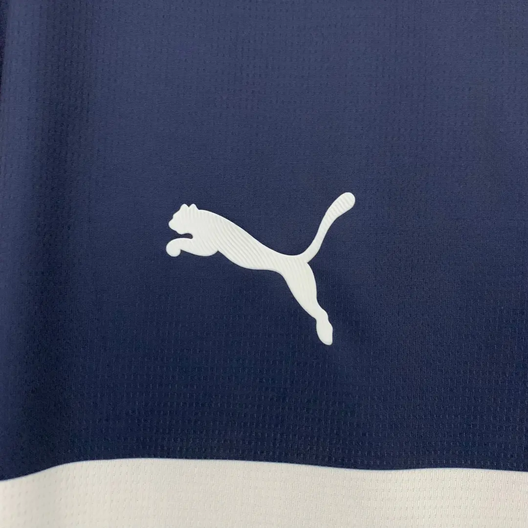 El logo blanco de Puma, mostrando la silueta del felino saltando, se sitúa sobre una tela texturizada de color azul marino, con una franja blanca visible en la parte inferior.