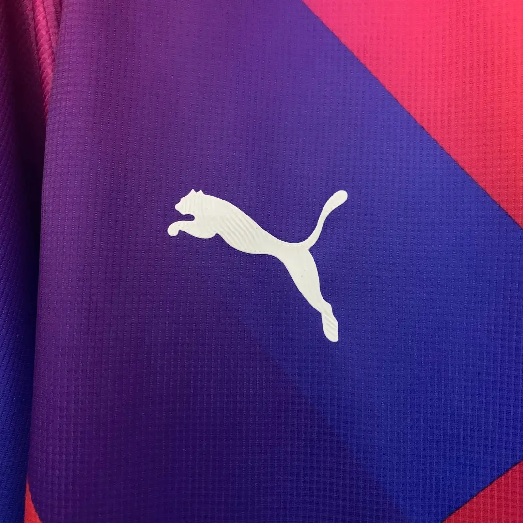 Primer plano de una camiseta deportiva de la marca Puma, mostrando su logo blanco sobre un fondo con un degradado de morado a azul y un detalle en rojo en la esquina superior derecha, con una textura acanalada.