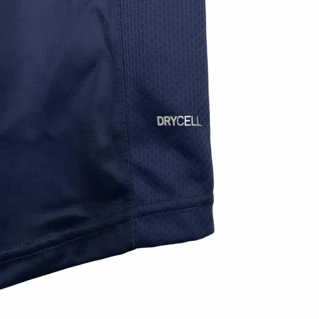 Primer plano de un tejido deportivo azul marino con la inscripción plateada 'DRYCELL', que destaca la tecnología de secado rápido y la textura transpirable de la prenda.