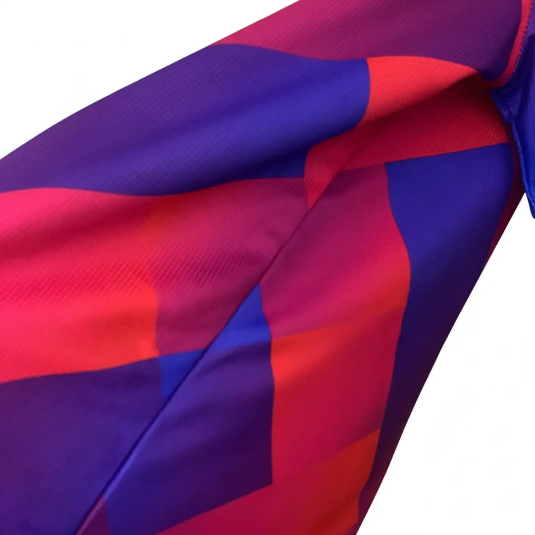 Primer plano de una tela deportiva con un patrón geométrico de bloques en tonos vibrantes de morado, azul eléctrico y rojo rosado, con una textura sutil visible.