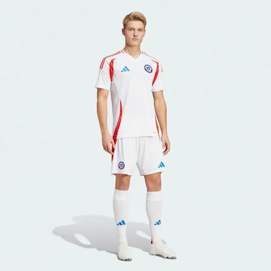 Modelo masculino vistiendo el uniforme de fútbol local blanco de Chile con detalles rojos de Adidas, que incluye camiseta, pantalón corto y medias, posando de frente sobre un fondo blanco liso.